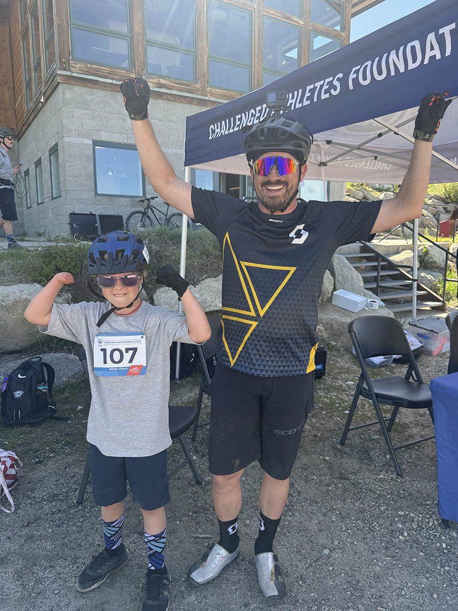 Steven and a young athlete throwing their arms up triumphantly at a Challenged Athletes Foundation event